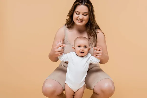 Positif mère taille plus tenant les mains de fille gaie isolé sur beige — Photo de stock
