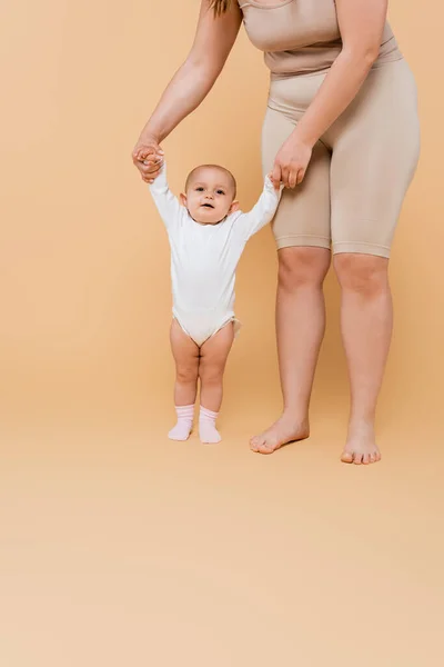 Plus size woman holding hands of baby daughter on beige background — Stock Photo