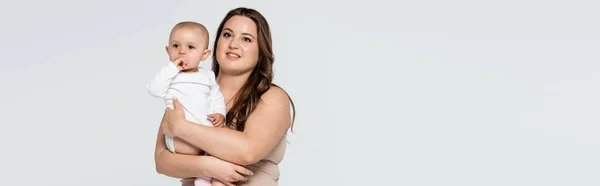 Sorridente plus size donna che tiene la bambina isolata sul grigio, banner — Foto stock