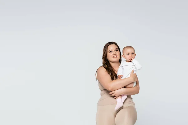 Mujer feliz con sobrepeso sosteniendo niño aislado en gris - foto de stock