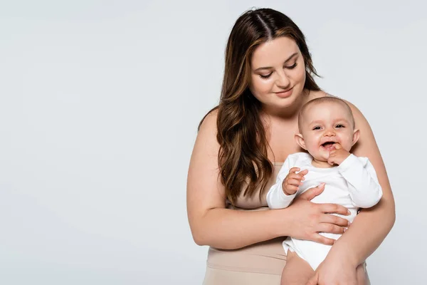 Glückliche Plus-Size-Frau hält fröhliches Baby isoliert auf grau — Stockfoto