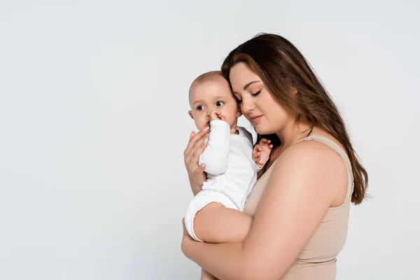 Pretty plus size mother hugging baby daughter isolated on grey — Stock Photo