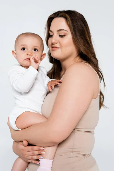 Smiling mother with overweight hugging baby girl isolated on grey — Stock Photo