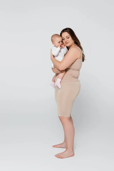 Junge Plus-Size-Frau umarmt Baby-Tochter auf grauem Hintergrund — Stockfoto