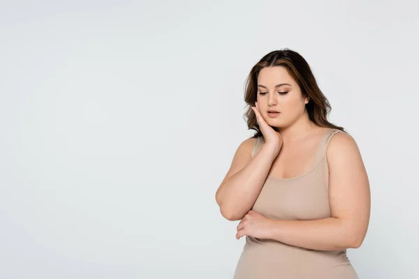 Mujer bonita con sobrepeso tocando la cara aislada en gris - foto de stock