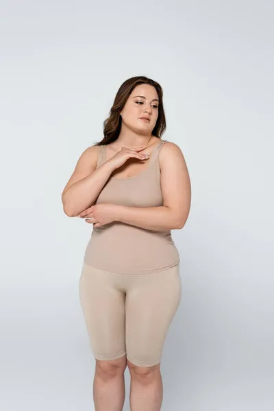 Mujer joven cuerpo positivo tocando pecho aislado en gris - foto de stock