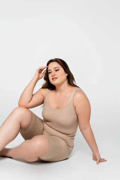 Mujer sonriente cuerpo positivo sentado sobre fondo gris - foto de stock