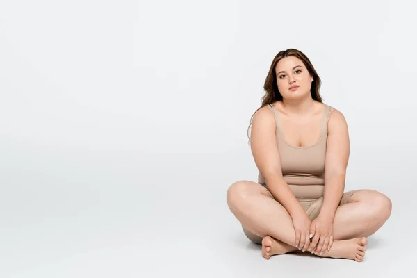 Mulher morena com sobrepeso sentado com pernas cruzadas em fundo cinza — Fotografia de Stock