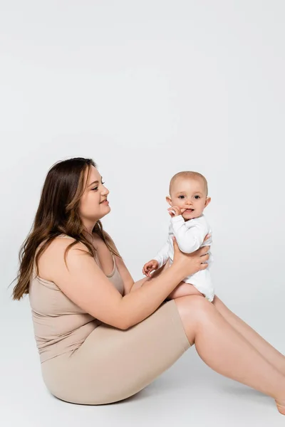 Bonita mujer de talla grande sosteniendo al niño con el dedo cerca de la boca sobre fondo gris - foto de stock