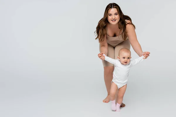 Feliz mujer de tamaño grande mirando a la cámara mientras toma de la mano de la niña sobre fondo gris - foto de stock