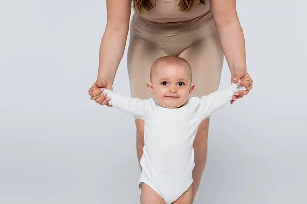 Baby girl holding hands of body positive mother isolated on grey — Stock Photo