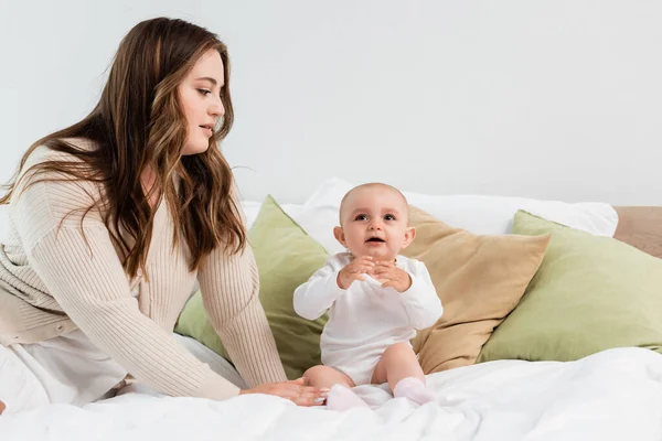 Joven madre de talla grande mirando a la niña en la cama en casa - foto de stock