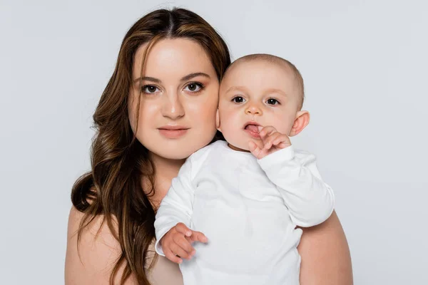 Pretty plus size woman looking at camera near baby daughter isolated on grey — Stock Photo