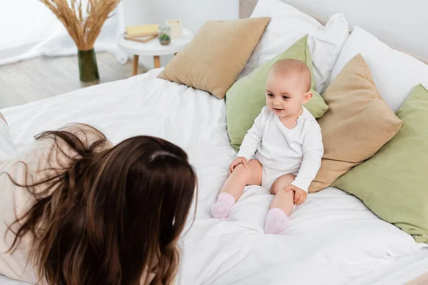 High angle view of young mother lying near baby daughter on bed — Stock Photo