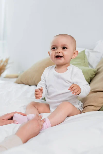 Fröhliches Babymädchen sitzt auf Bett in der Nähe von Mamas Händen — Stockfoto