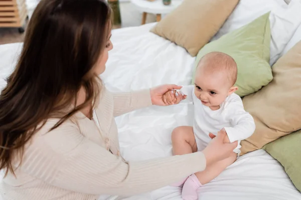 High angle view of mother holding hands of baby daughter on bed — Stock Photo