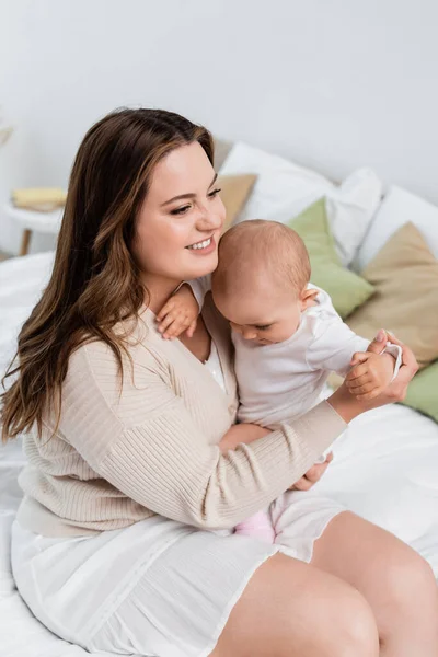 Glückliche Plus-Size-Mutter umarmt Baby-Mädchen zu Hause auf dem Bett — Stockfoto