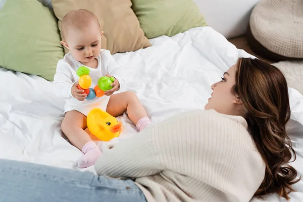 Plus size mother lying near baby daughter with toys on bed — Stock Photo