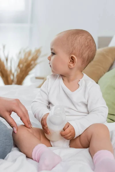 Donna che tocca la bambina con una bottiglia di latte sul letto — Foto stock
