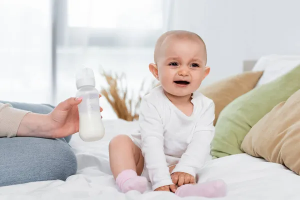 Mulher segurando mamadeira com leite perto da filha alegre na cama — Fotografia de Stock