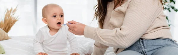 Mother with overweight holding spoon while feeding baby on bed, banner — Stock Photo