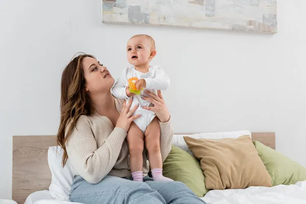 Mulher feliz com sobrepeso segurando criança com brinquedos na cama — Fotografia de Stock