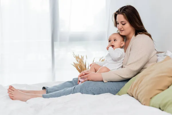 Corps positif mère positive touchant les jambes de bébé fille sur le lit — Photo de stock