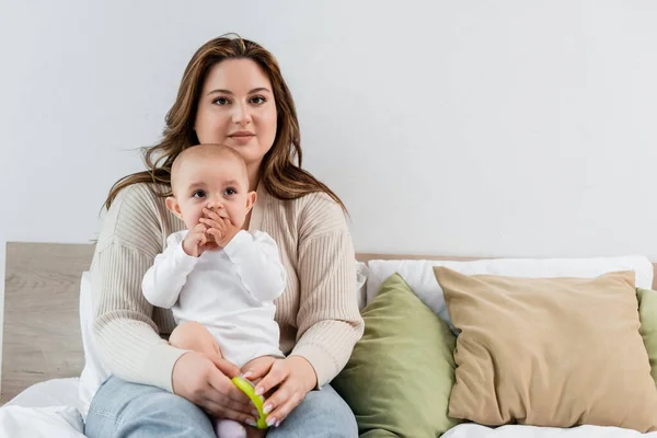 Hübsche Plus-Size-Mutter hält Spielzeug in der Nähe der kleinen Tochter auf dem Bett — Stockfoto