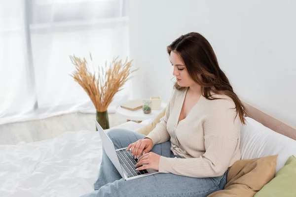 Bella donna con sovrappeso utilizzando il computer portatile sul letto — Foto stock