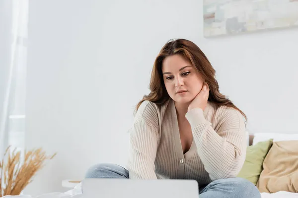 Joven freelancer con sobrepeso mirando el portátil borroso en casa - foto de stock