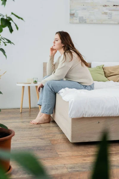 Боковой вид молодой позитивной женщины, сидящей дома на кровати — стоковое фото