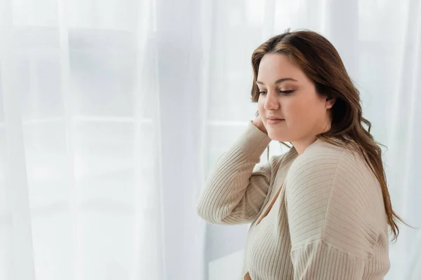 Hübsche körperlich positive Frau, die zu Hause neben Gardinen steht — Stockfoto