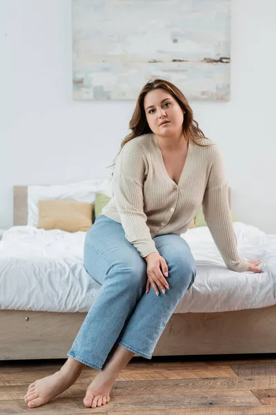 Jolie femme positive de corps en vêtements décontractés regardant la caméra sur le lit — Photo de stock