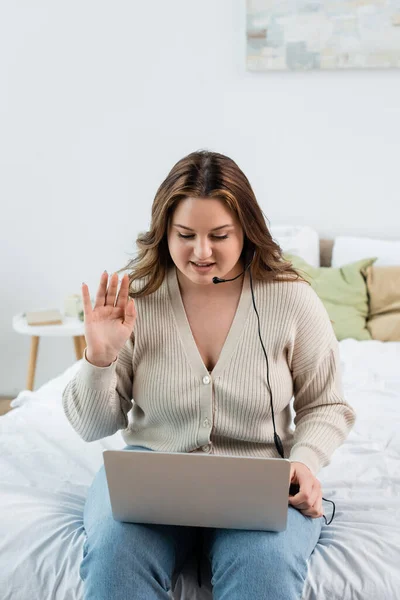 Più il collaboratore esterno di dimensioni in cuffia che ha videochiamata su computer portatile in camera da letto — Foto stock