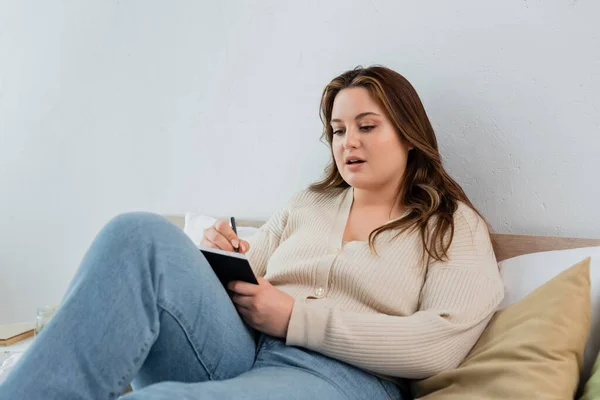 Jeune femme plus la taille écrivant sur ordinateur portable sur le lit — Photo de stock