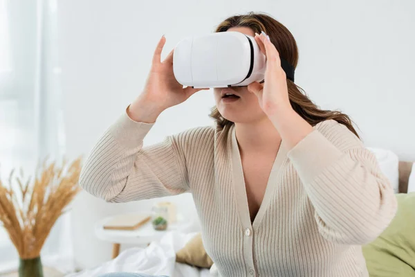 Mujer joven con sobrepeso usando auriculares de realidad virtual en casa - foto de stock
