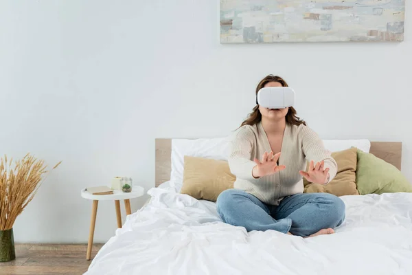 Брюнетка плюс розмір жінка грає у гарнітуру віртуальної реальності на ліжку — стокове фото