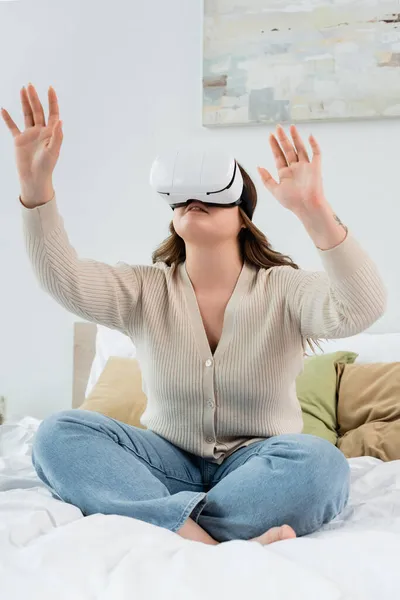 Молодая позитивная женщина, играющая в гарнитуру VR, сидя на кровати — стоковое фото