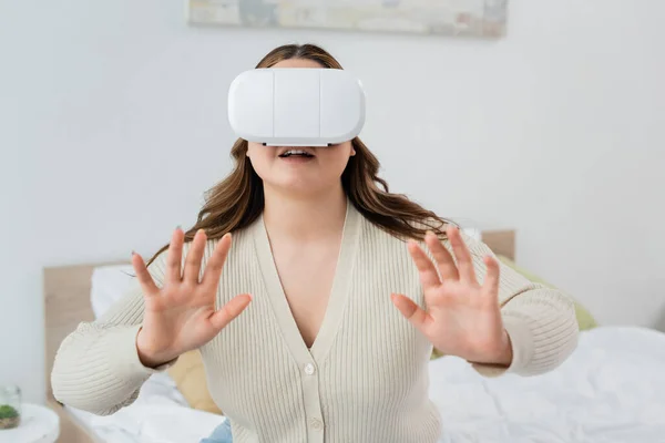 Усміхнена жінка з іграми з надмірною вагою у гарнітурі віртуальної реальності в спальні — стокове фото