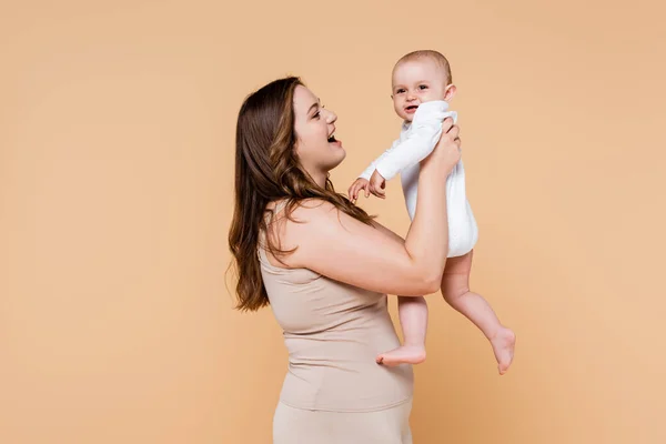 Eccitato più dimensioni mamma tenendo sorridente bambino isolato su beige — Foto stock