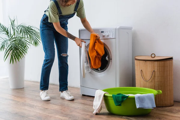 Ausgeschnittene Ansicht einer Hausfrau, die Kleidung in die Waschmaschine in der Nähe von Waschschüssel und Wäschekorb legt — Stockfoto