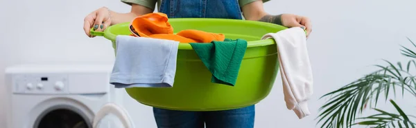 Cropped view of woman holding laundry bowl near blurred washing machine, banner — Stock Photo