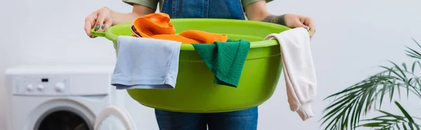 Vista recortada de la mujer sosteniendo un recipiente de lavandería cerca de la lavadora borrosa, pancarta - foto de stock