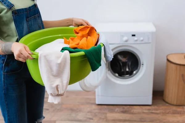 Teilbild einer Hausfrau, die Wäsche in der Nähe einer verschwommenen Waschmaschine zu Hause hält — Stockfoto