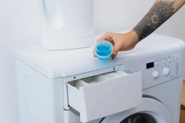 Vue recadrée de femme tatouée tenant capuchon avec détergent liquide près de la machine à laver — Photo de stock