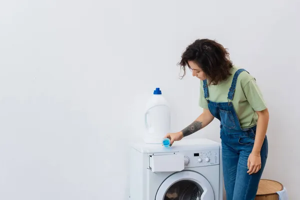 Morena mujer añadiendo detergente líquido en la lavadora - foto de stock