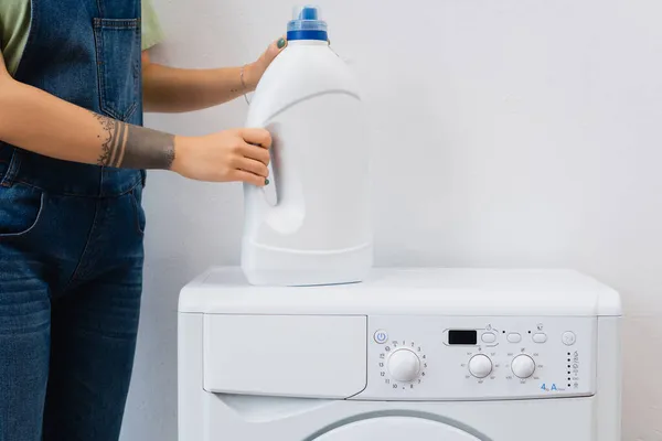 Partial view of tattooed woman holding bottle of detergent near washing machine — Stock Photo