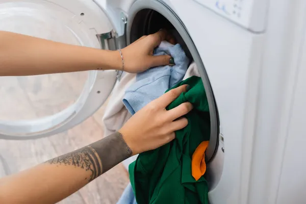Частковий вид татуйованої жінки, що вкладає білизну в пральну машину — стокове фото