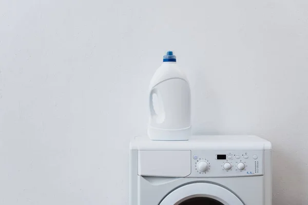Garrafa de detergente na máquina de lavar roupa perto da parede branca — Fotografia de Stock