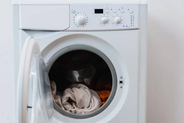 Wäsche in offener Waschmaschine neben weißer Wand — Stockfoto
